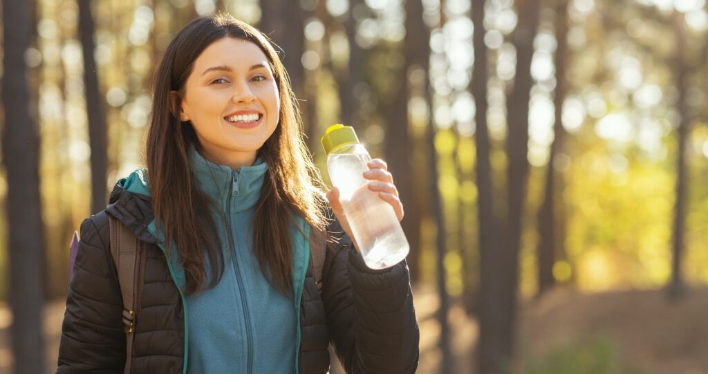 Smiling young woman drinking water while hiking
